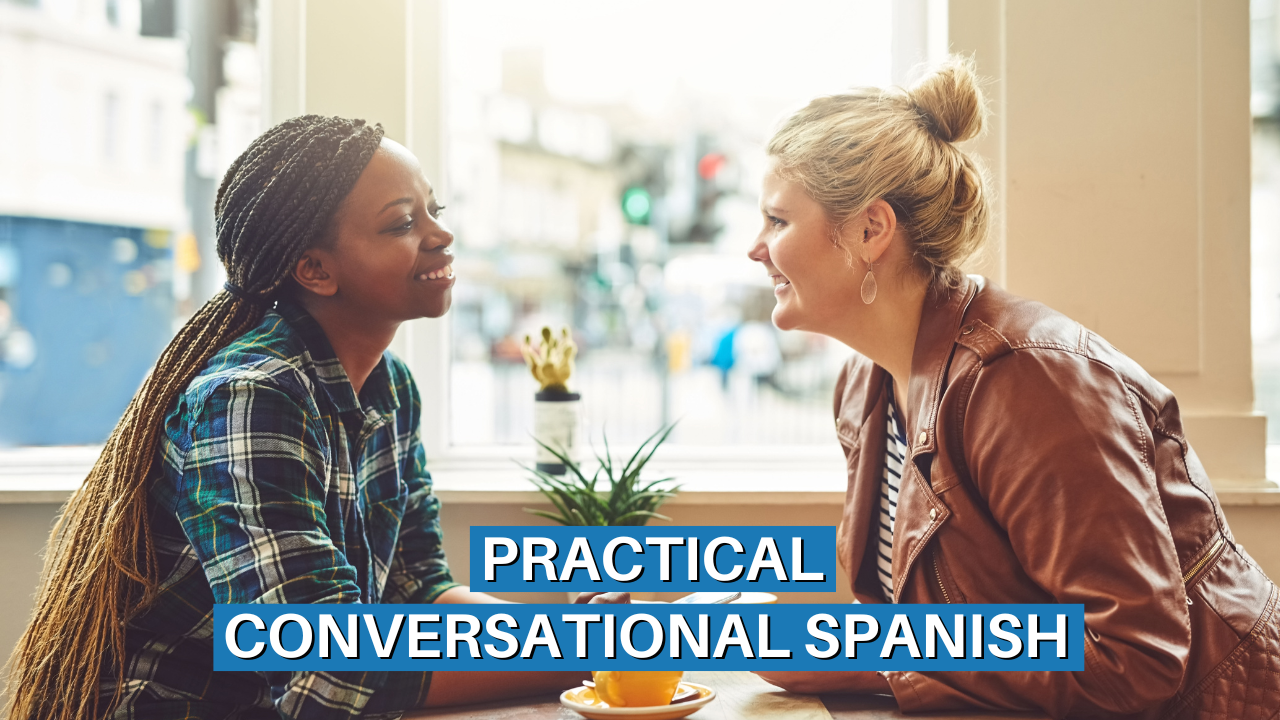 Two friends talking and smiling at a table, while practicing speaking Spanish together.